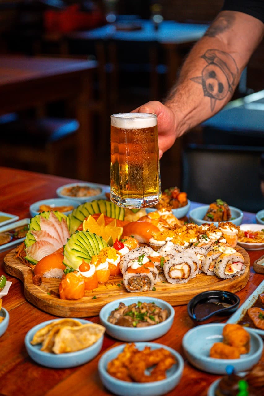 Mesa de rodízio do Tio Panda, com tábua de sushi e um chopp sendo servido